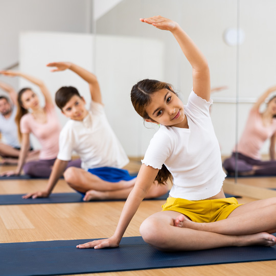 Family in a group fitness studio sitting on yoga mats holding a yoga pose